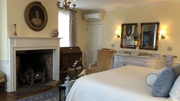 A bedroom with a large bed, a fireplace, a chandelier, a mirror, and a dresser.
