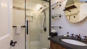 A modern bathroom with a glass-enclosed shower, a wooden vanity with a marble countertop, and a large mirror above the sink.