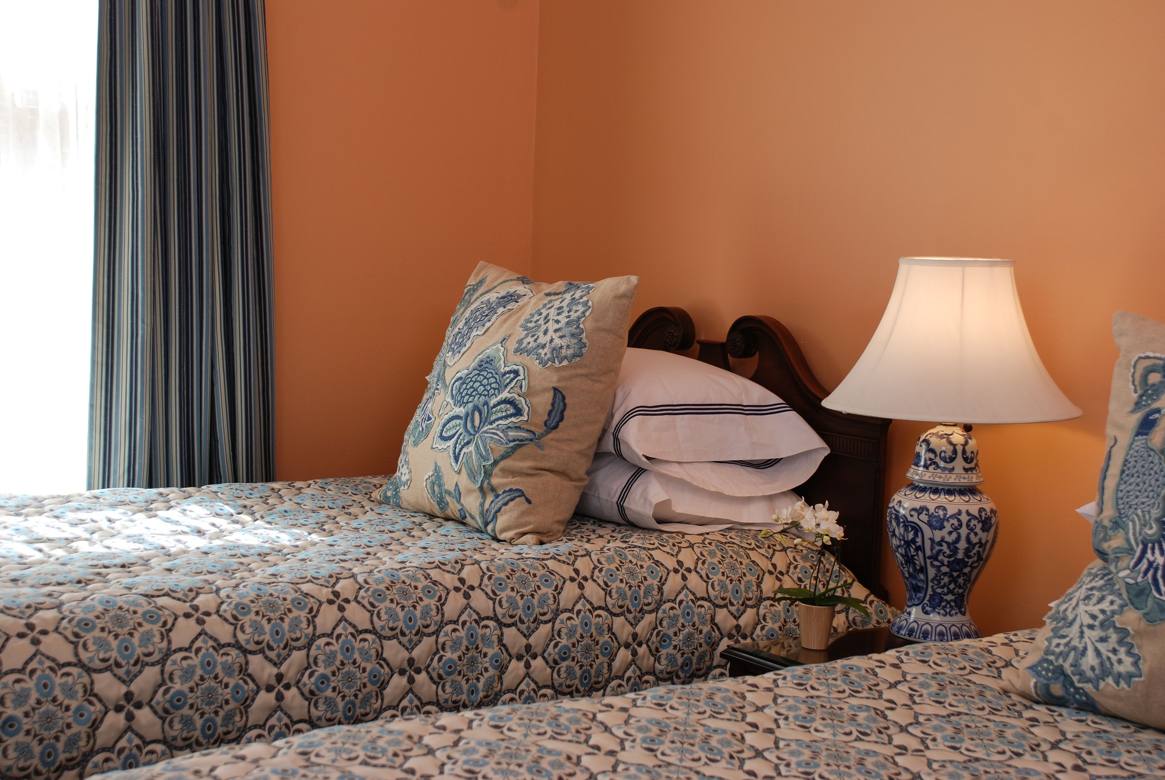 Quarto de hotel com cama, almofadas, abajur e um vaso.