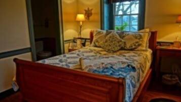 A wooden bed with a patterned bedspread, a nightstand with a lamp, and a window with a view of the outside.