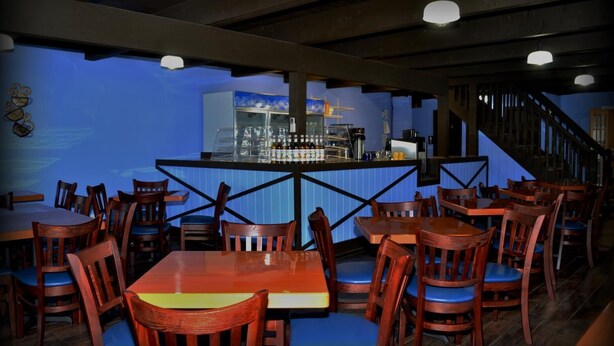 A restaurant with wooden tables and chairs, a bar area with a glass display case, and a staircase leading to an upper level. - Wayne Inn (Honesdale)