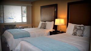 A hotel room with two beds, a window with a view, a bedside table with a lamp, and a decorative pillow. - Wayne Inn (Honesdale)