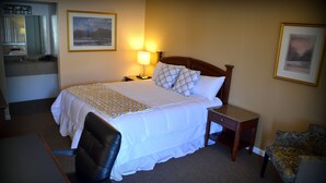 A hotel room with a bed, bedside table, lamp, chair, desk, and a small table with a lamp. - Wayne Inn (Honesdale)