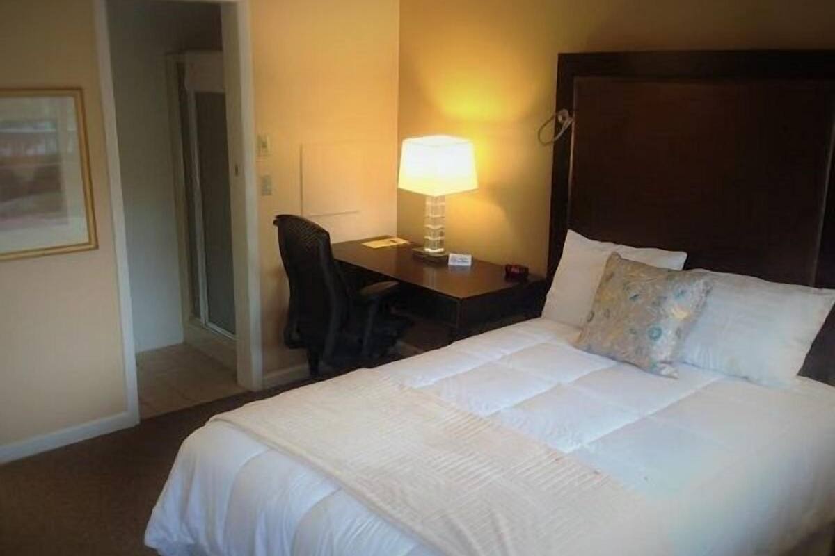 A hotel room with a large bed, a desk with a lamp, and a chair.
