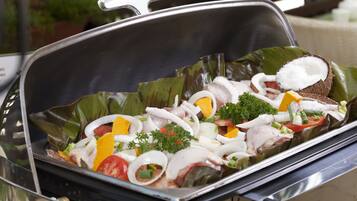 Un buffet proposant une variété d’aliments, notamment des viandes, des légumes et des accompagnements, servis sur un plateau avec un couvercle.