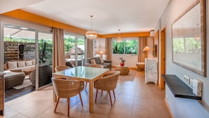 Un vaste espace de vie avec une porte-fenêtre coulissante donnant sur un balcon, une table à manger avec des chaises en osier, un canapé et une table basse.