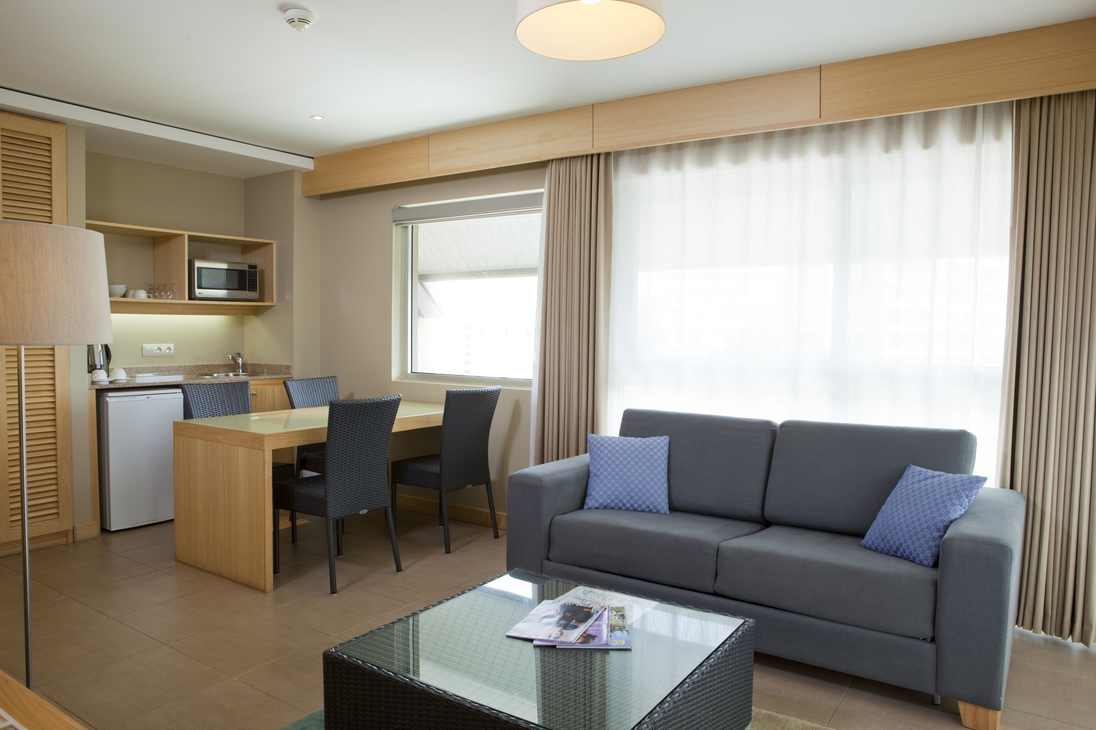 Una habitación de hotel moderna con comedor, sofá y mesa de centro de vidrio.
