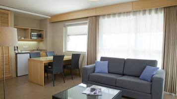 Una habitación de hotel moderna con comedor, sofá y mesa de centro de vidrio.