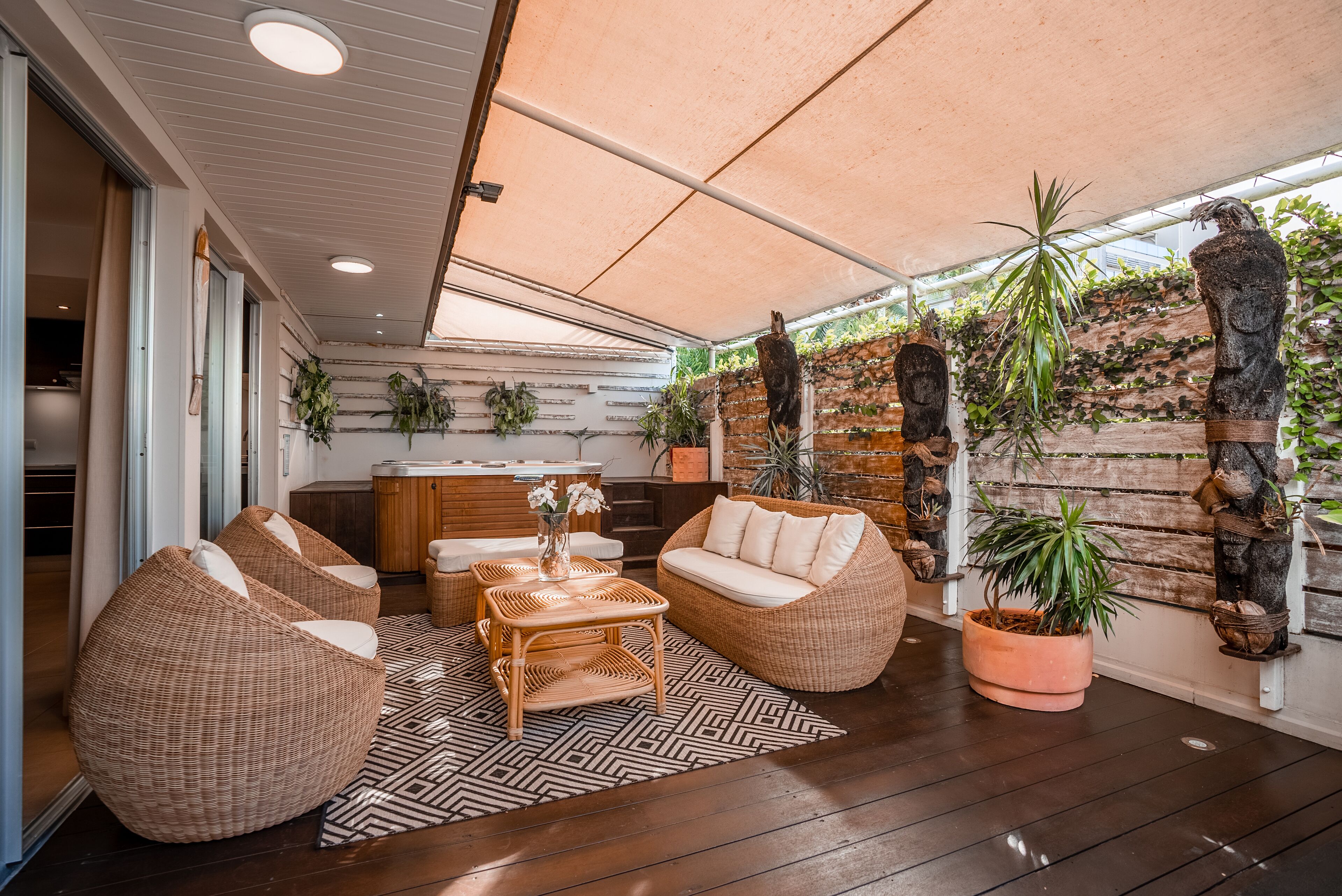 A cozy outdoor seating area with wicker furniture, a patterned rug, and potted plants.