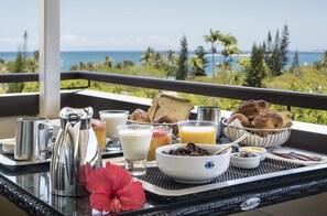 Een ontbijtplateau met koffie, melk, sap en gebak op een balkon met uitzicht op een prachtig landschap.