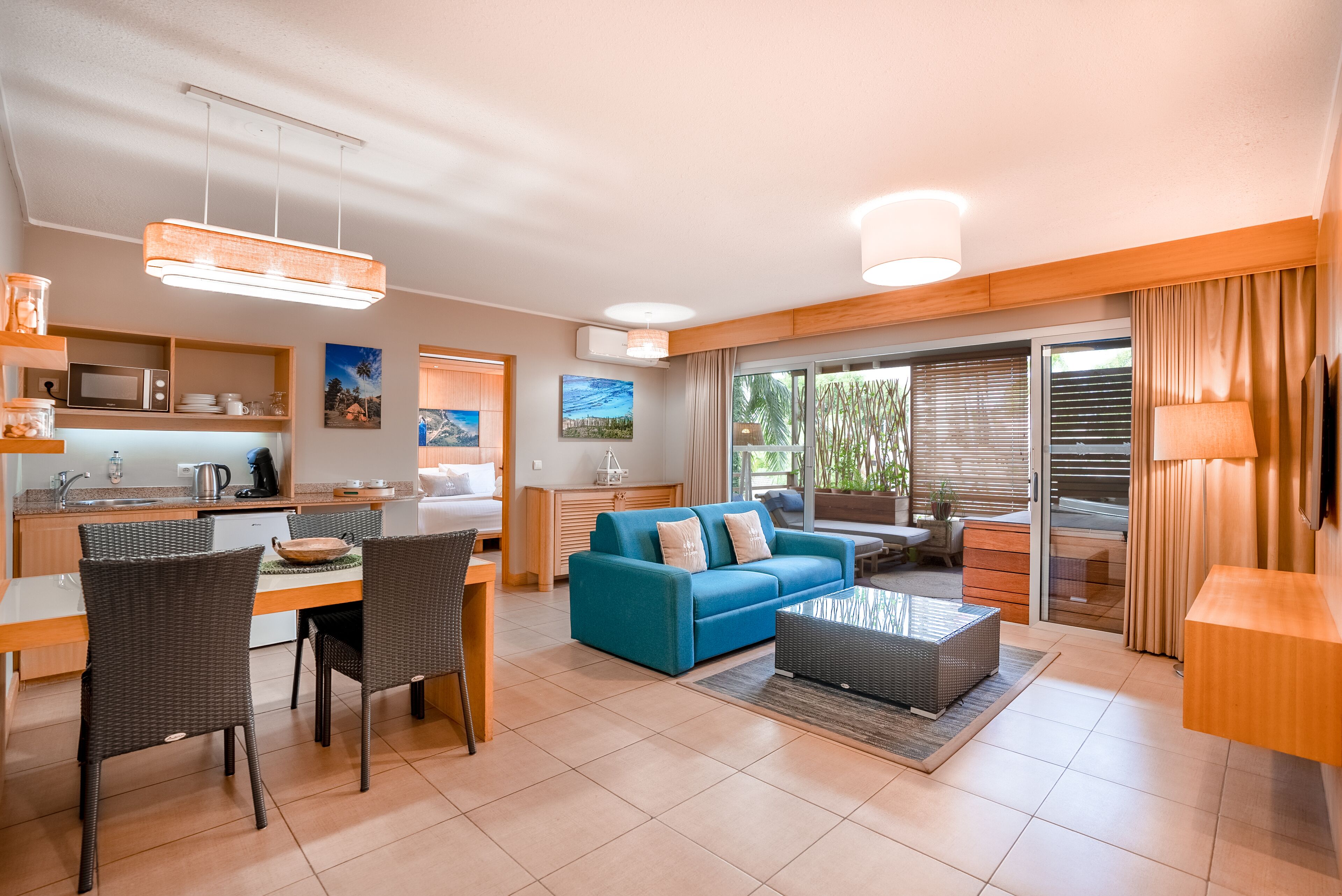 A modern living room with a blue sofa, dining area, kitchen, and large sliding glass doors to a balcony.