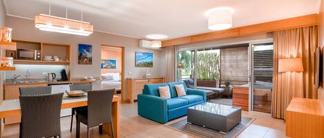 A modern living room with a blue sofa, dining area, kitchen, and large sliding glass doors to a balcony.