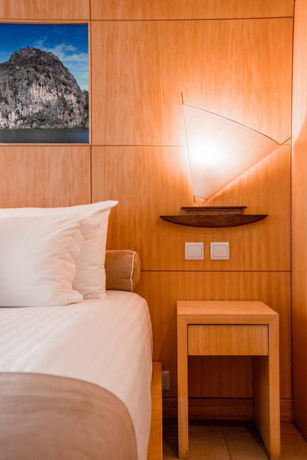Habitación de hotel con cama, mesita de noche, estante en la pared y una fotografía de una montaña.