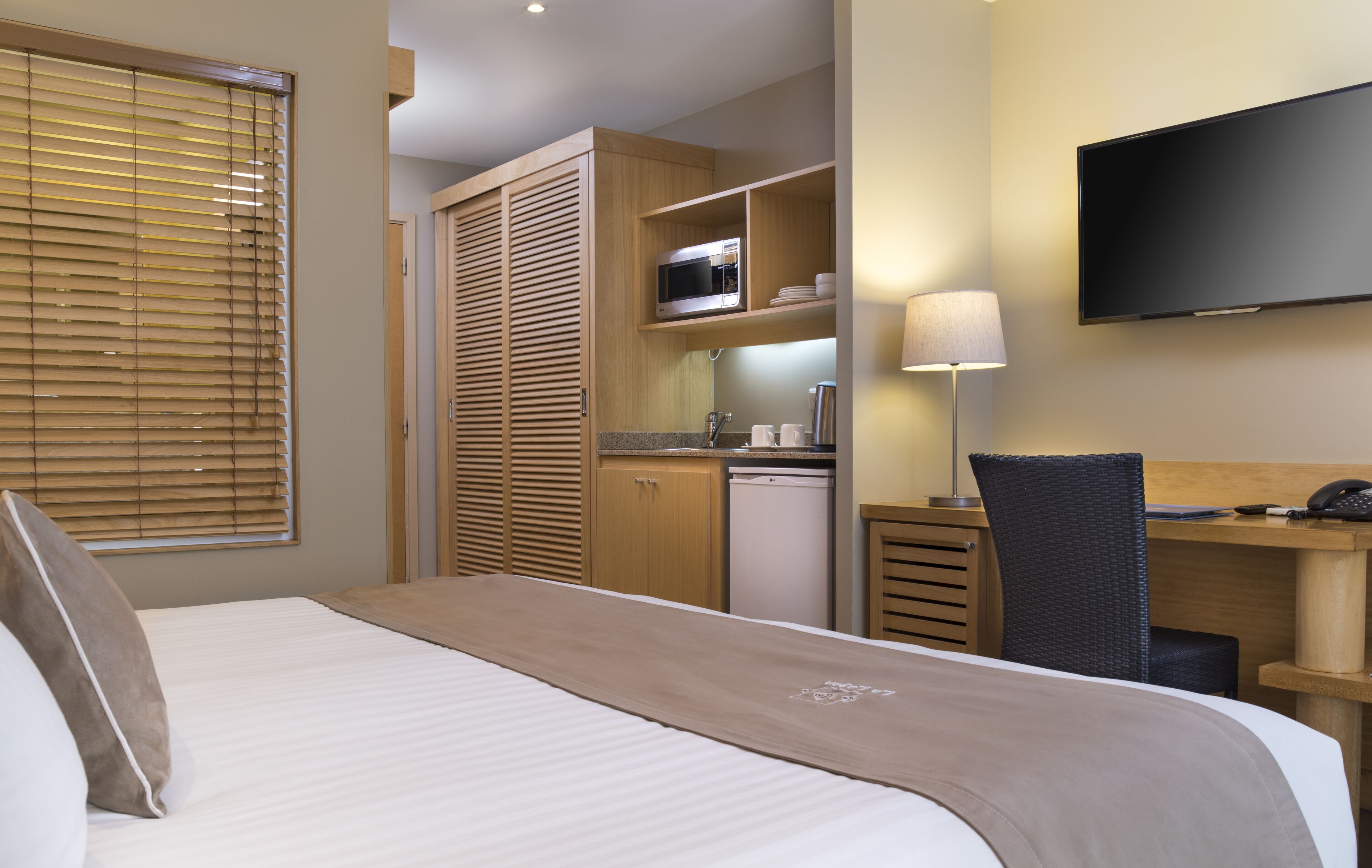 A hotel room with a bed, a desk, a chair, a television, a microwave, and a kitchenette.