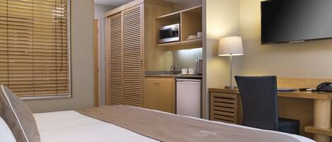 A hotel room with a bed, a desk, a chair, a television, a microwave, and a kitchenette.