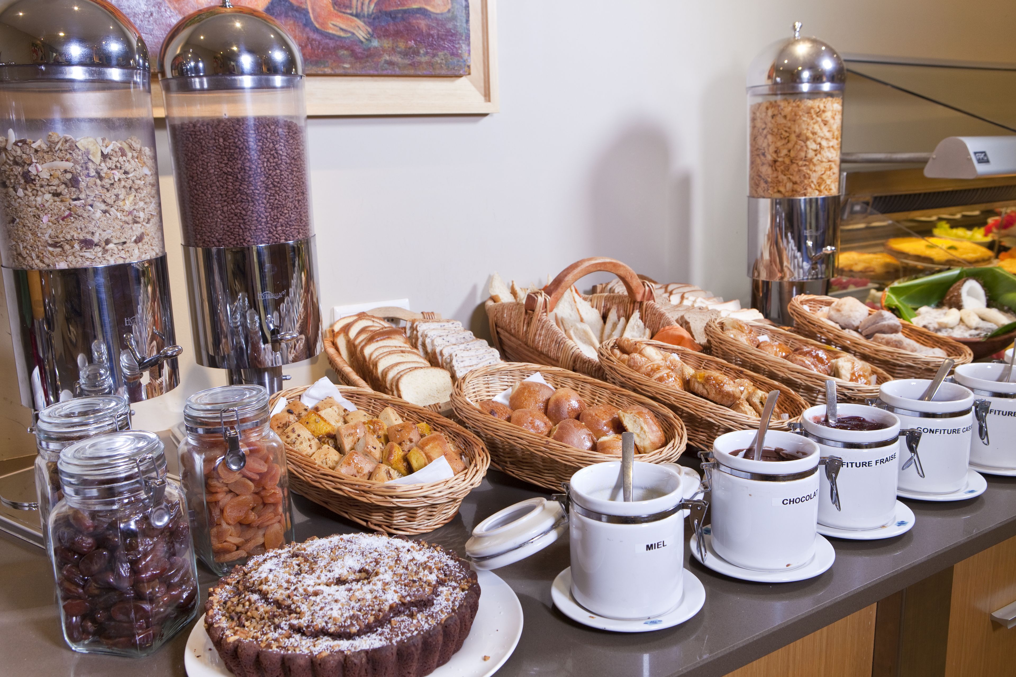 A buffet with various food items, including breads, pastries, and jars of spreads.