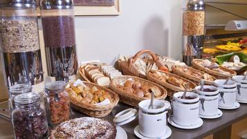 A buffet with various food items, including breads, pastries, and jars of spreads.