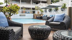 Un espace extérieur avec une piscine, des meubles en osier, une table en verre et des plantes en pot.