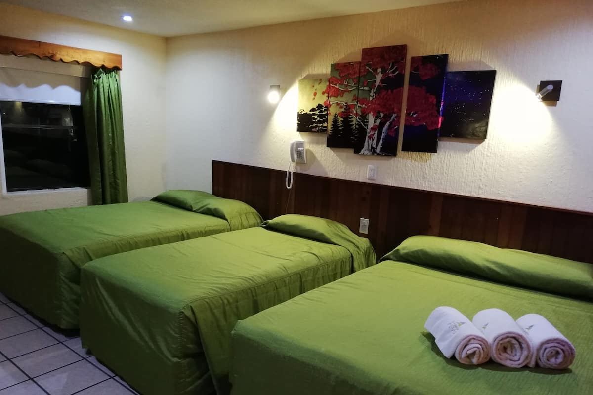 A hotel room with two single beds, a wooden headboard, a wall-mounted phone, and three paintings.