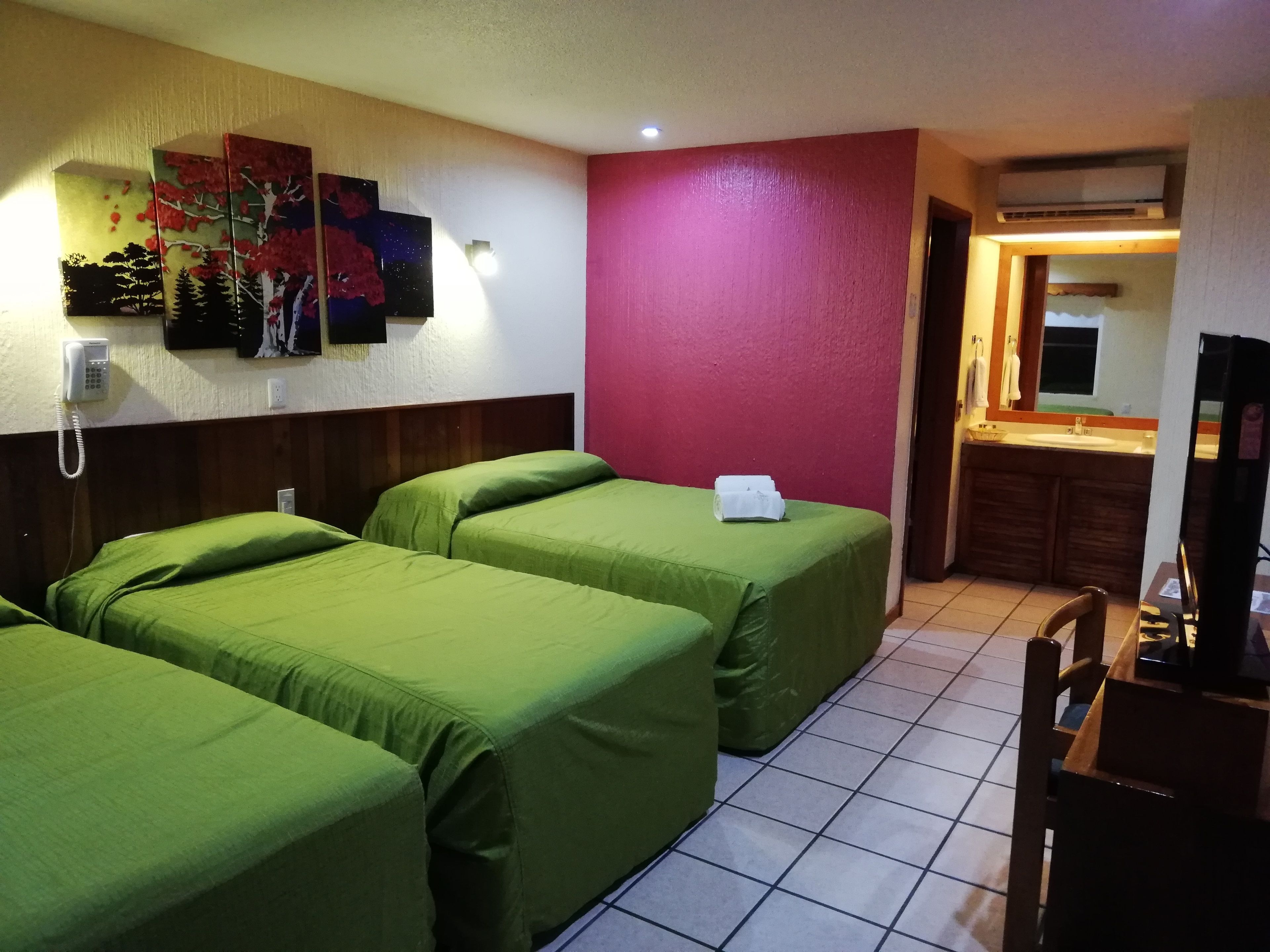 Une chambre d’hôtel avec deux lits simples, un petit bureau, un miroir et une salle de bain visible à travers une porte ouverte.