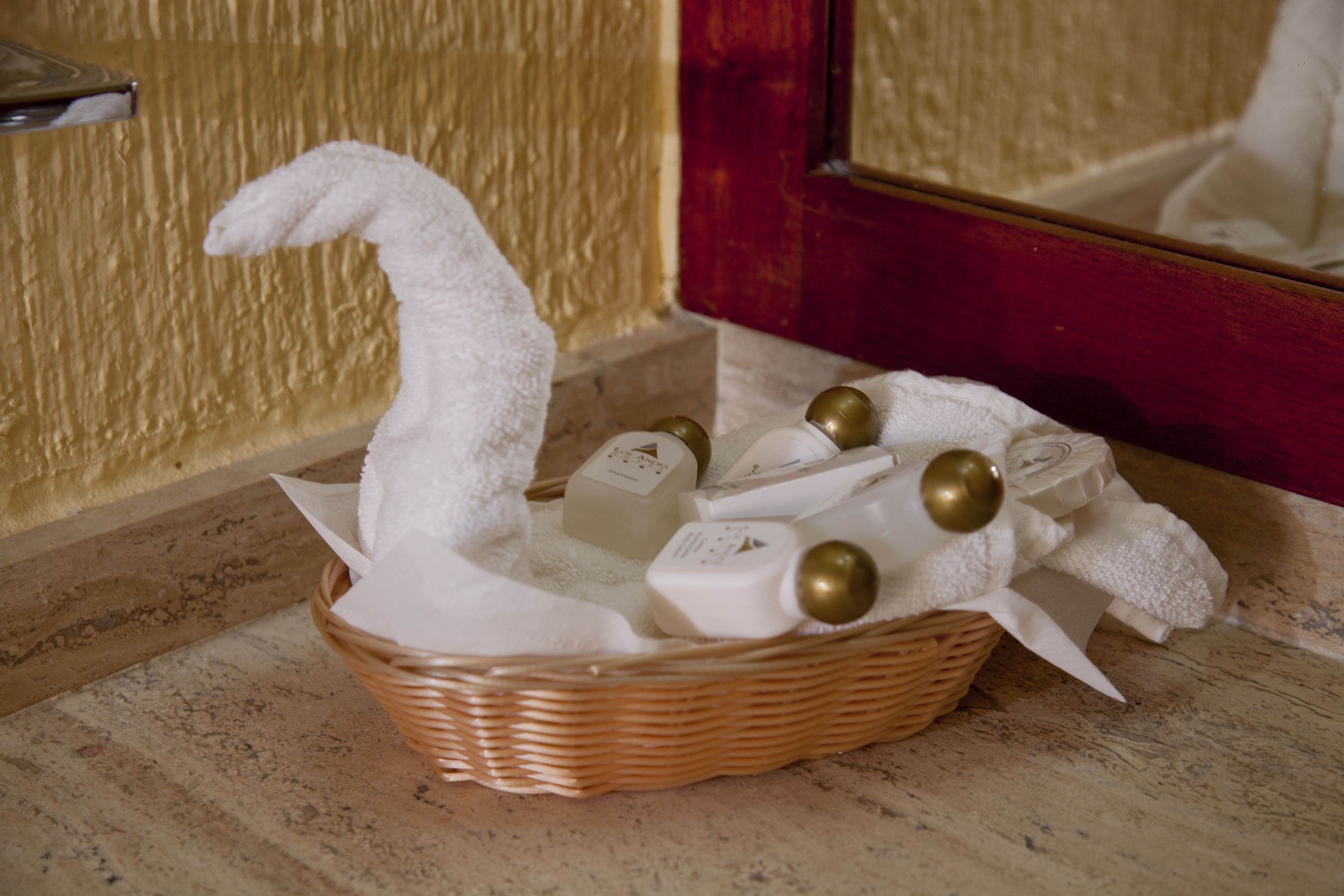 Una cesta de mimbre con artículos de aseo y una toalla blanca con forma de cisne sobre una encimera de mármol.