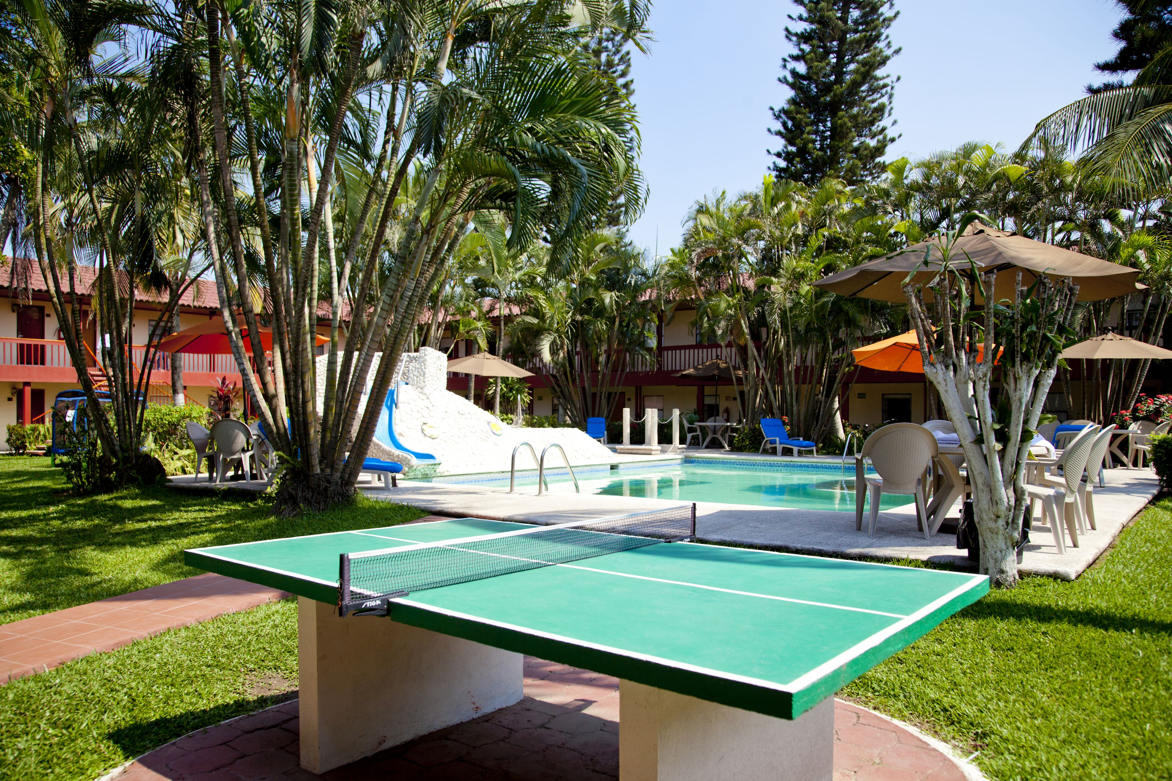 A pool table in a resort area with a pool, lounge chairs, and palm trees.