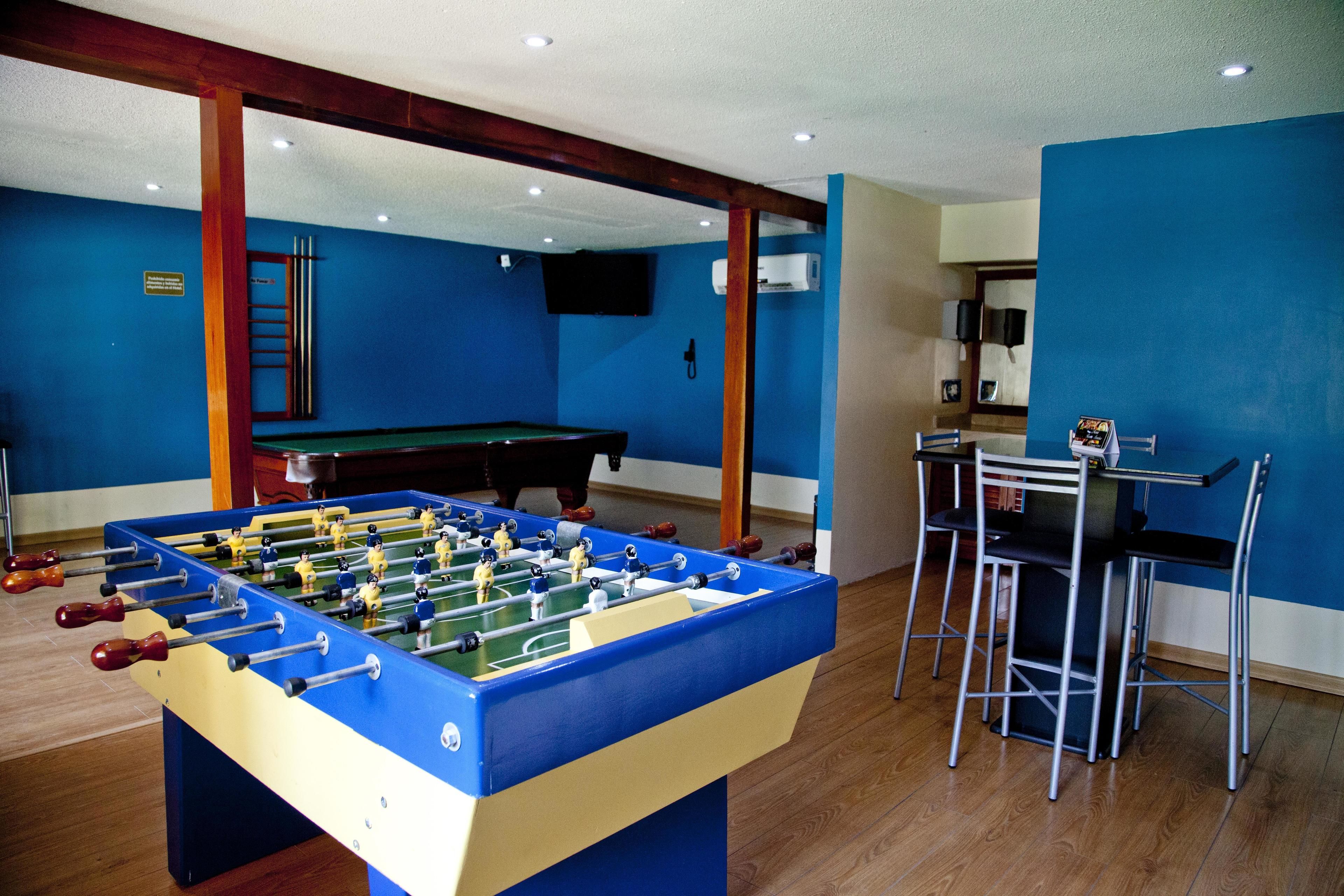 A room with a foosball table, a pool table, and a bar area with stools.