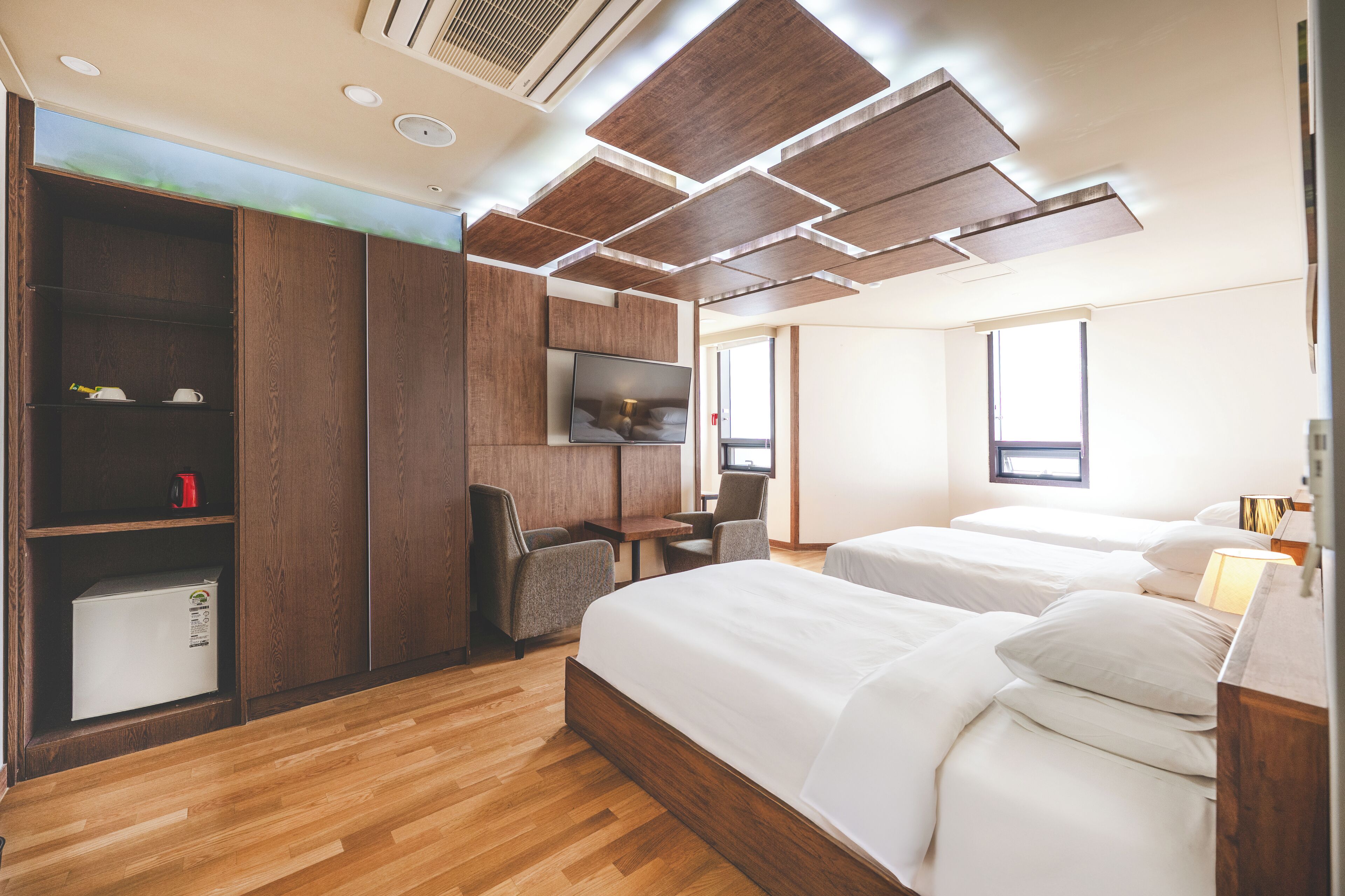 Ein modernes Hotelzimmer mit Holzboden, zwei Betten, einem Schreibtisch und einem Kleiderschrank.
