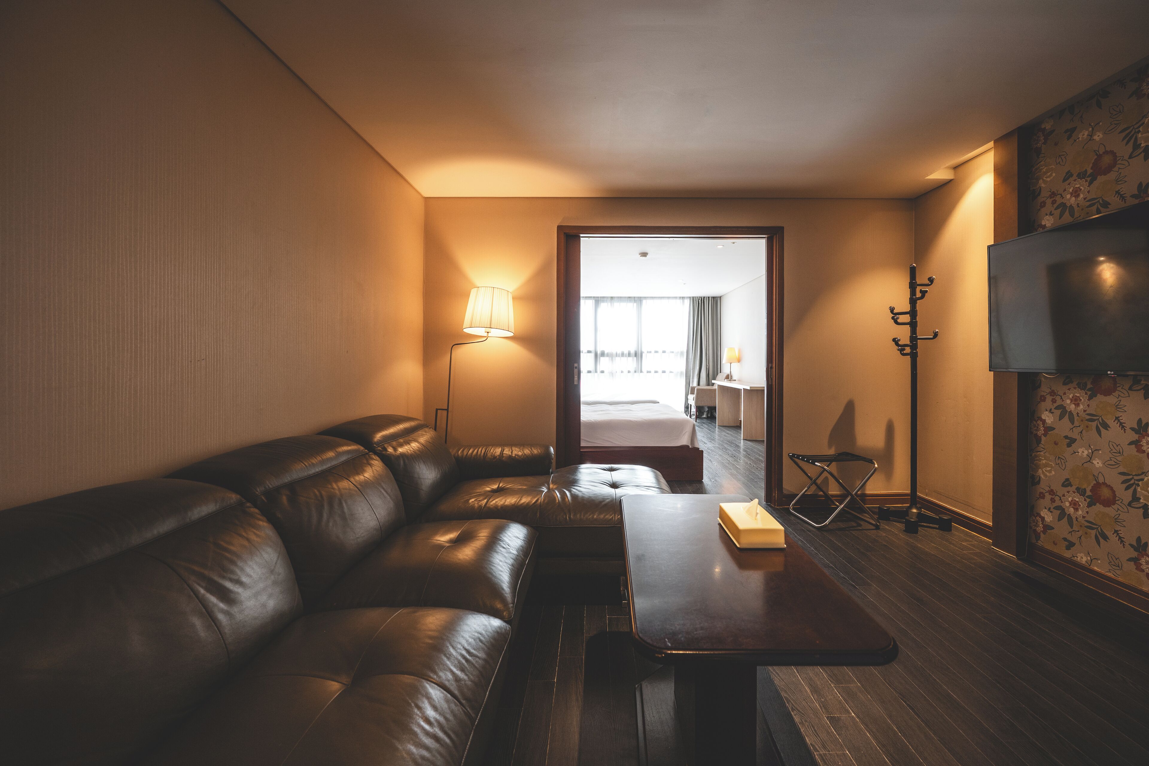 Een moderne hotelkamer met een leren bank, een houten salontafel, een flatscreen televisie en een lamp.