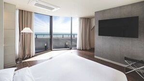 A modern hotel room with a large bed, a flat-screen TV mounted on the wall, and a balcony with a view of the sea. - Sunset Hotel (Busan)
