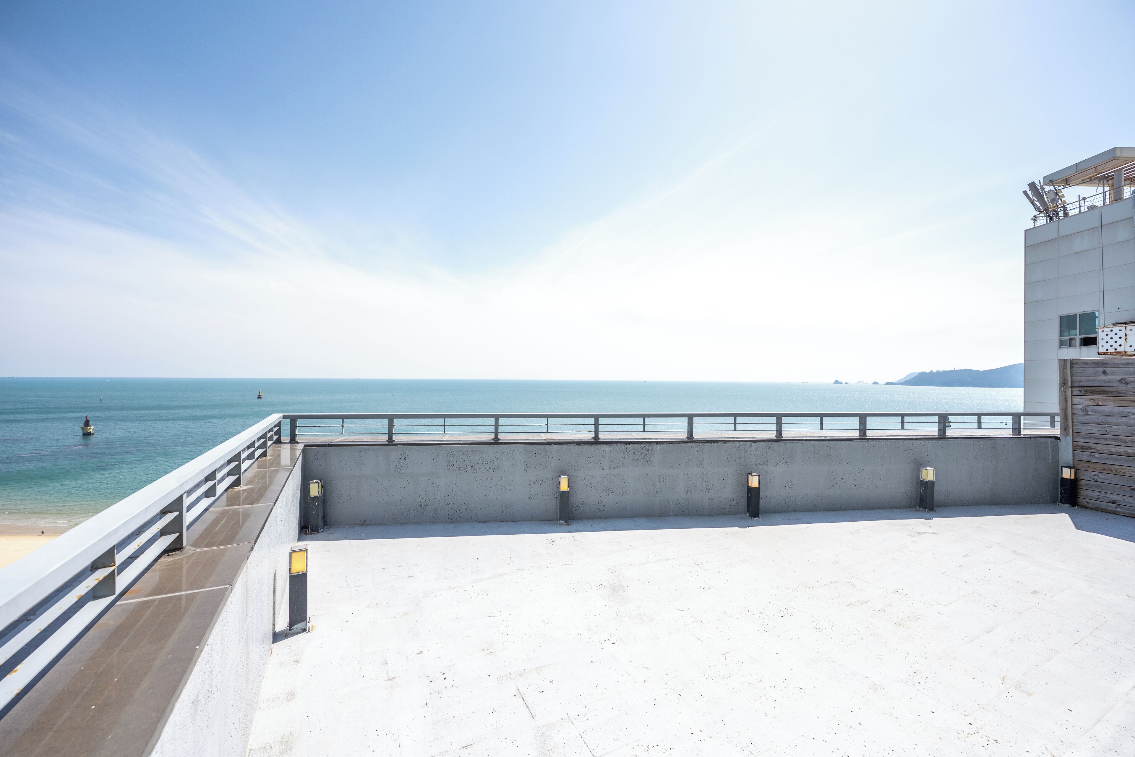 Una terraza en la azotea con piso de concreto, barandilla y vista al océano.