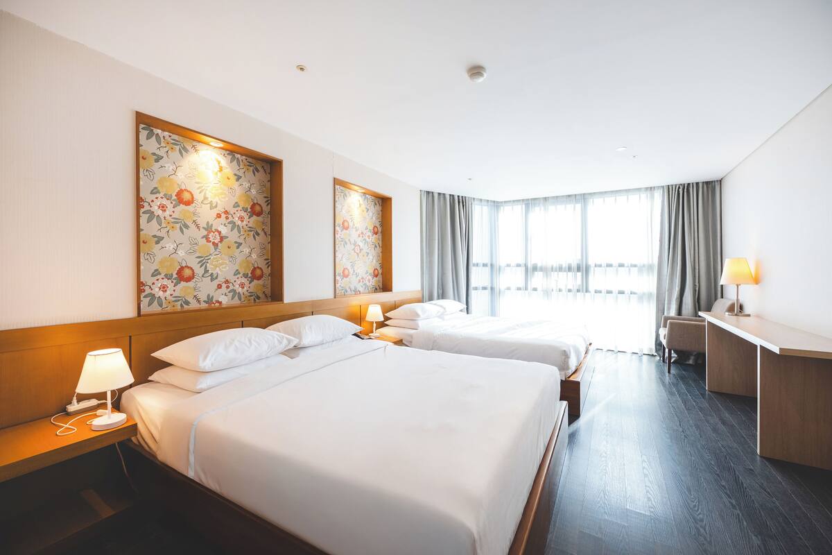 A hotel room with two beds, a desk, and a large window with curtains.