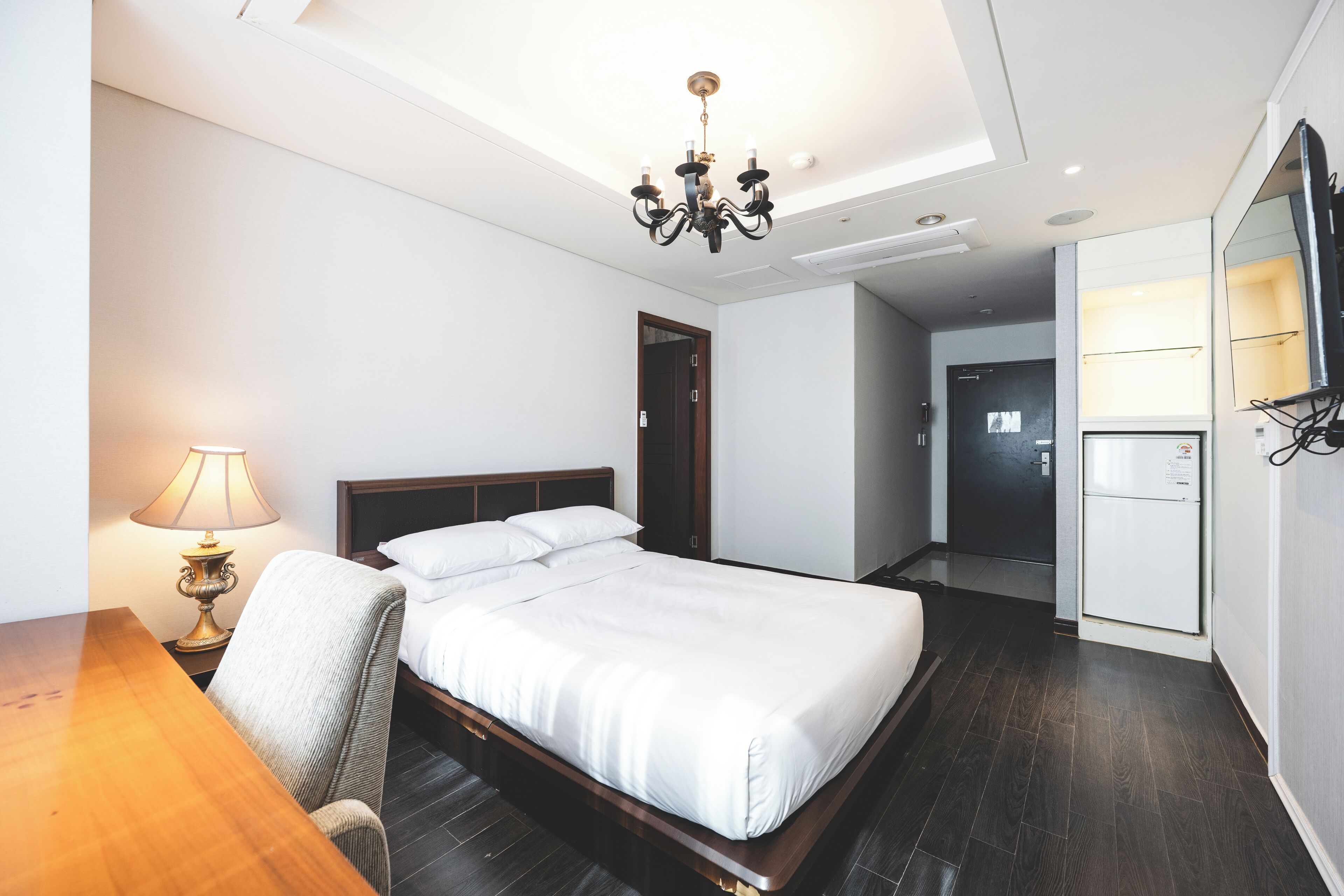 Een hotelkamer met een bed, een bureau, een stoel, een lamp, een televisie en een koelkast.