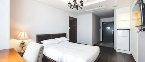 A hotel room with a bed, a desk, a chair, a lamp, a TV, and a refrigerator.