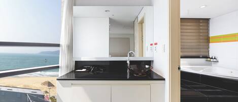 Un baño moderno con encimera negra, armarios blancos y vistas a la playa y al océano.