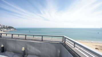 A coastal view from a balcony with a railing, overlooking a beach and the sea.