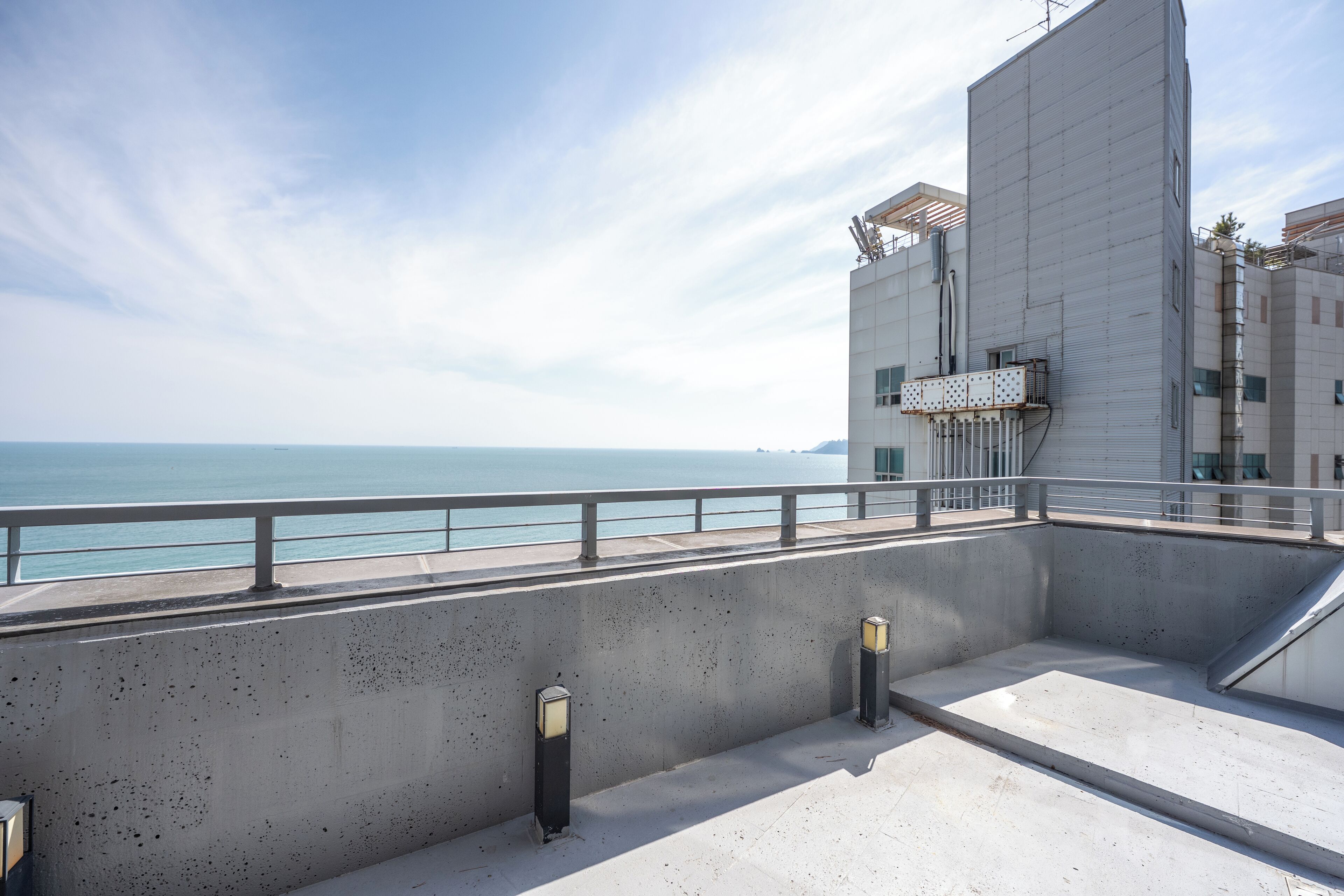 A rooftop terrace with a concrete floor, metal railing, and two wall-mounted lights.