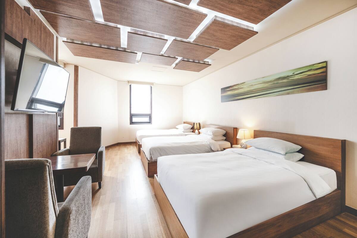 A hotel room with three beds, a TV, a desk, and a painting on the wall.
