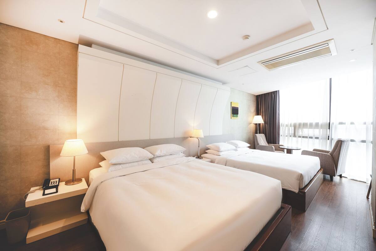 A hotel room with two beds, a desk, a chair, and a large window.