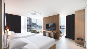 A modern hotel room with two beds, a TV mounted on a wooden panel, and a view of the city and sea. - Sunset Hotel (Busan)