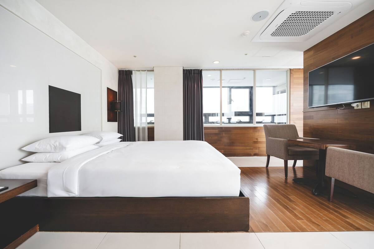 A modern hotel room with a large bed, a desk, a chair, and a TV mounted on the wall.