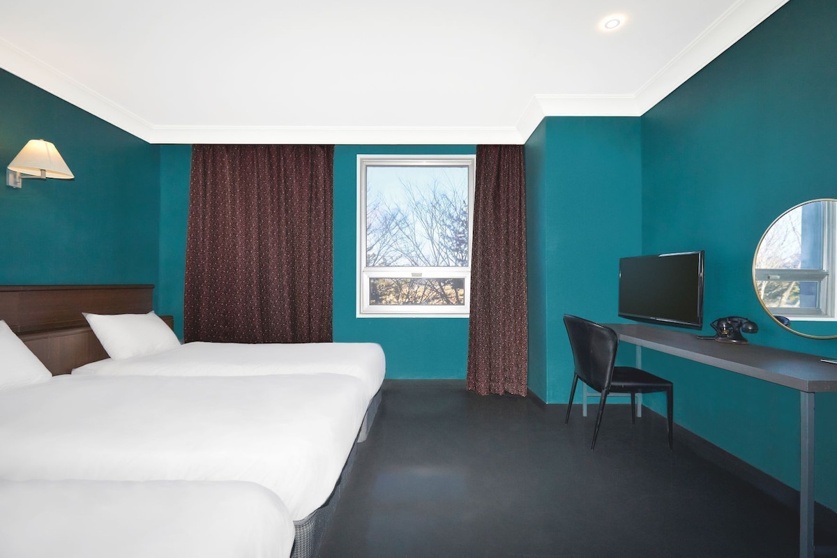 A hotel room with two beds, a desk with a chair, a television, and a window with curtains.