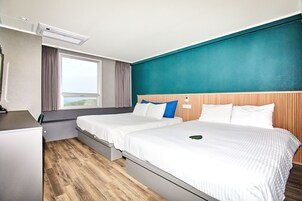 Hotellihuone, jossa on kaksi sänkyä, työpöytä, ikkuna verhoilla ja näkymä ulos.