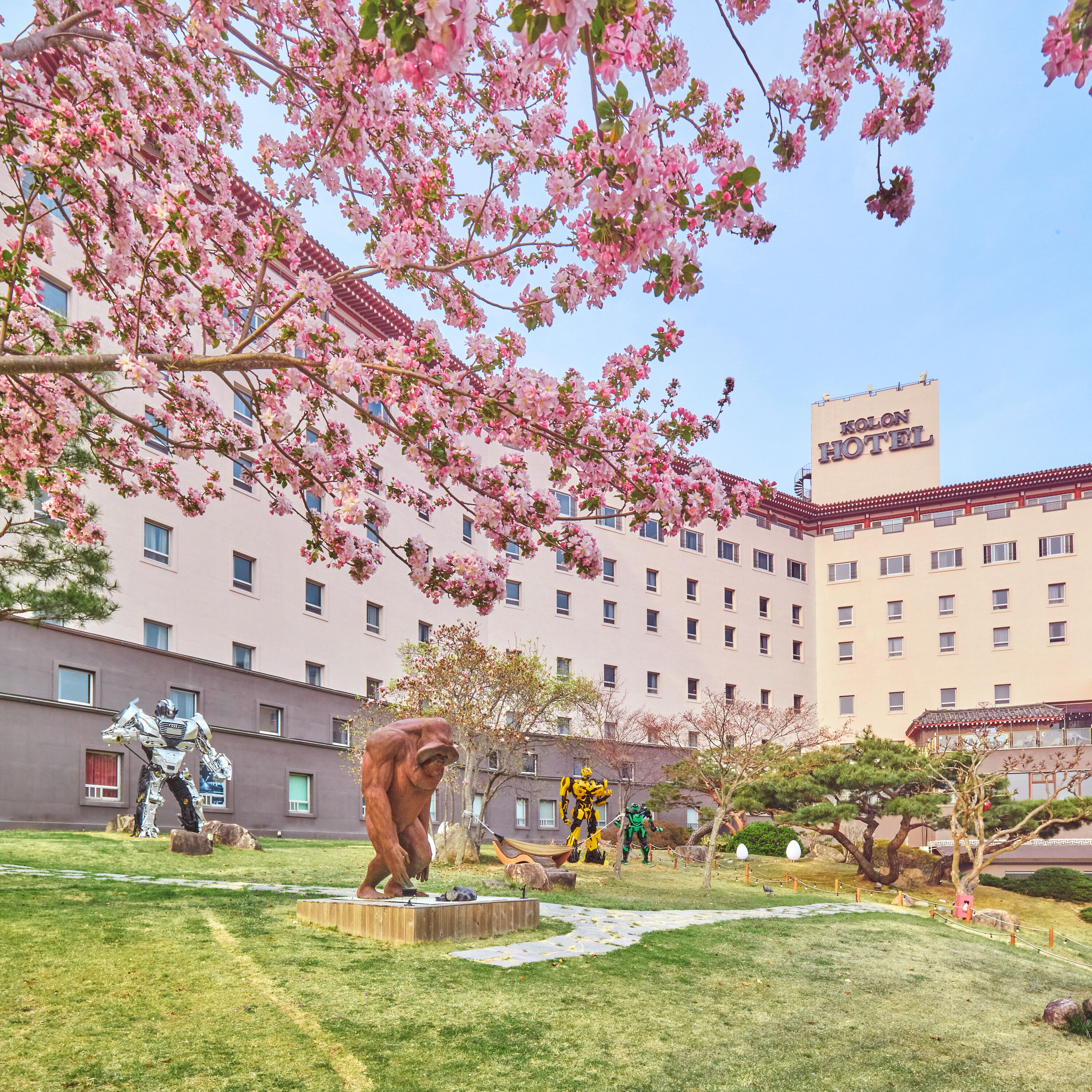 A hotel with a large building, a garden with sculptures, and cherry blossoms.