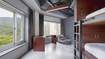 A modern room with bunk beds, a desk, and a view of greenery.