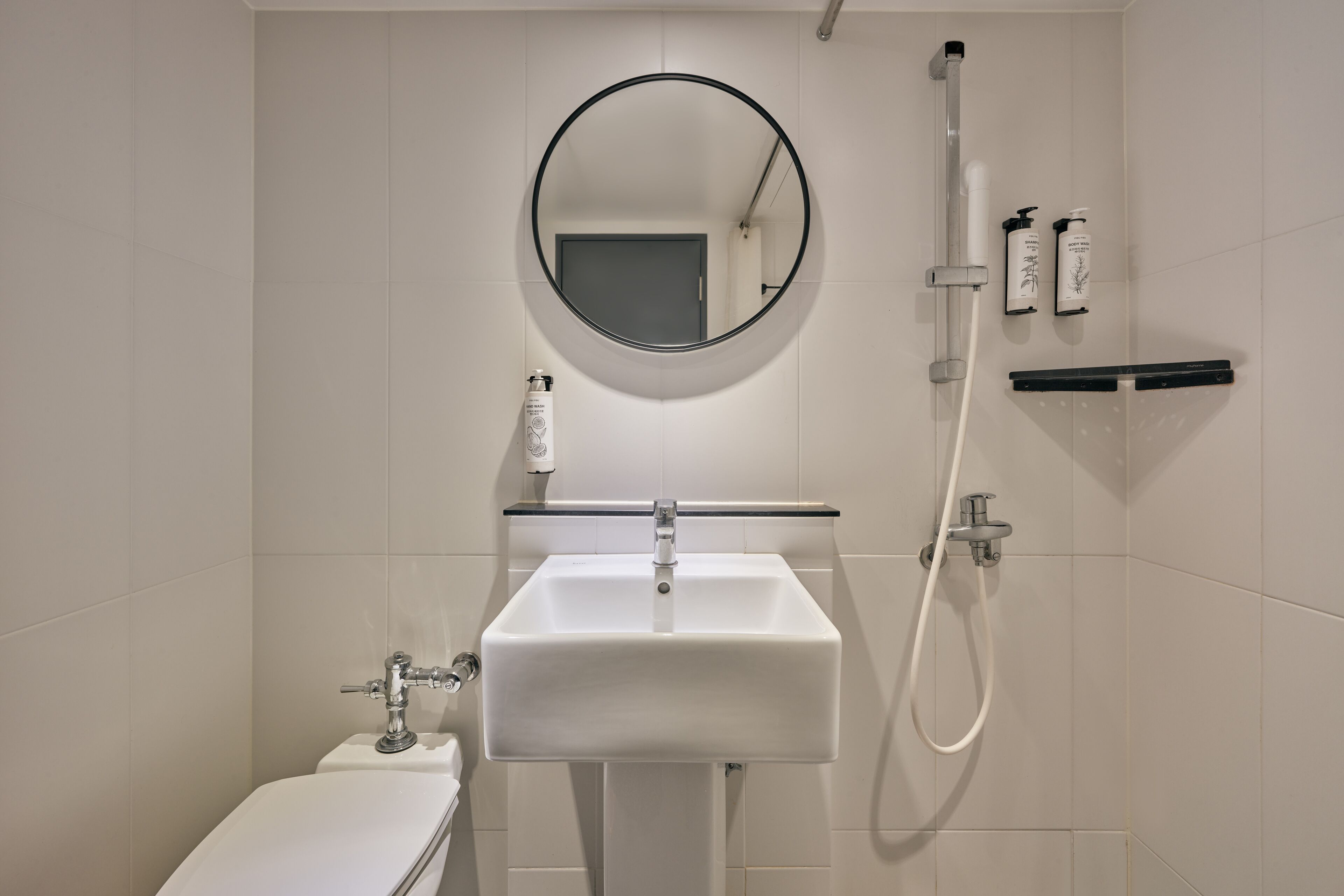 A modern bathroom with a white sink, a round mirror, and a handheld showerhead.