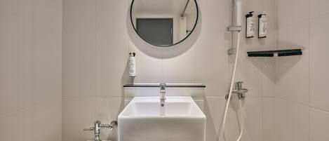 A modern bathroom with a white sink, a round mirror, and a handheld showerhead.