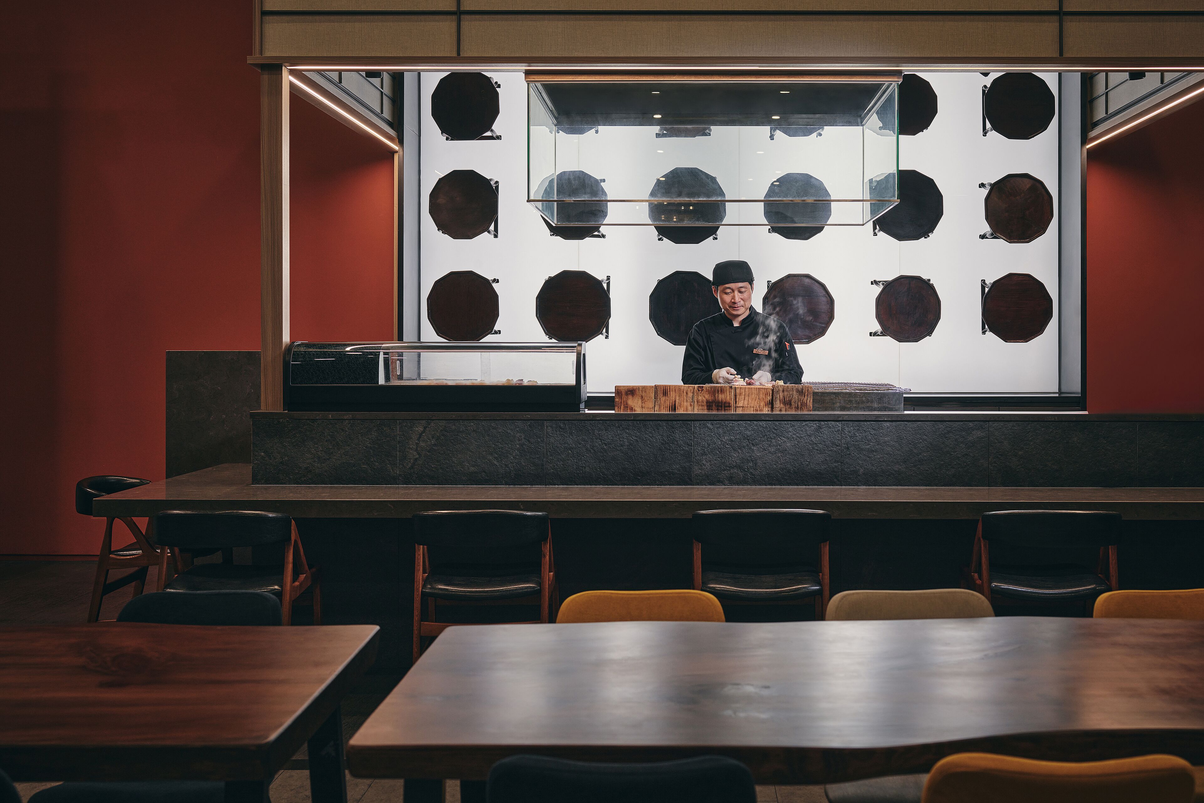 A restaurant with a chef preparing food, a display of wooden bowls, and several tables and chairs.