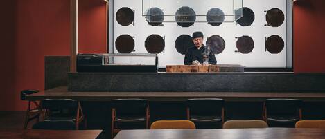 A restaurant with a chef preparing food, a display of wooden bowls, and several tables and chairs.