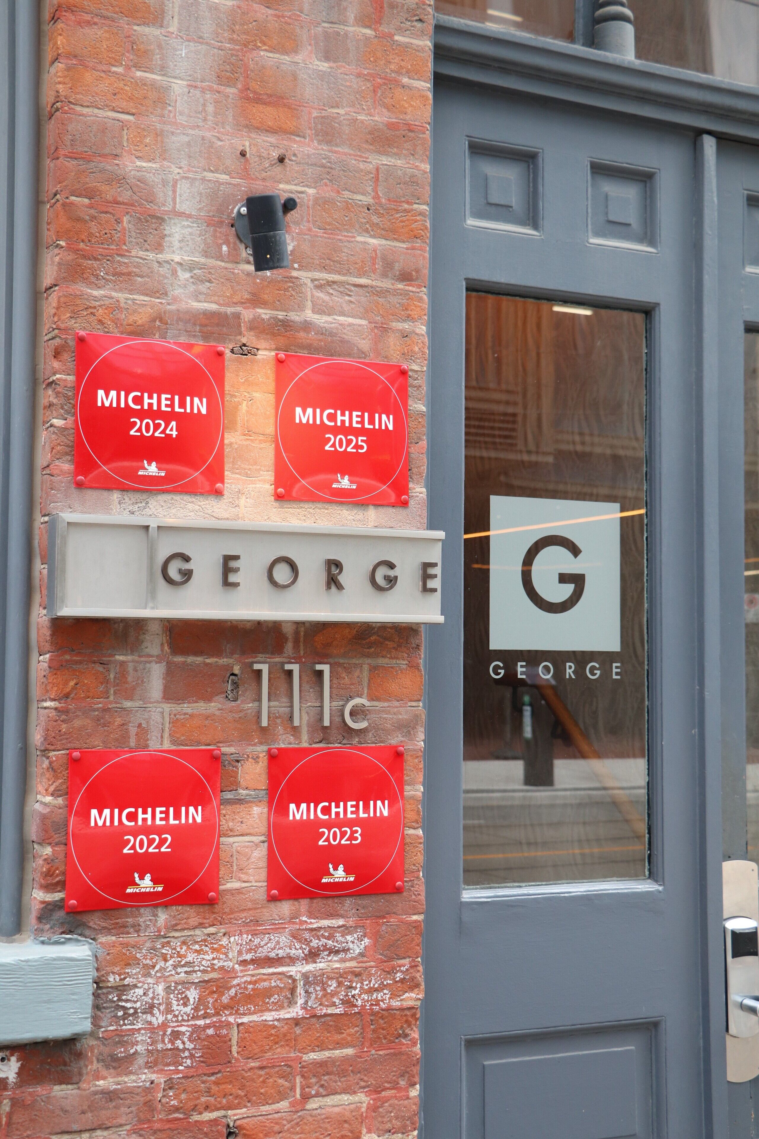 En murstensbygning med skilt for 'GEORGE' og Michelin-stjerner for 2022, 2023, 2024 og 2025.